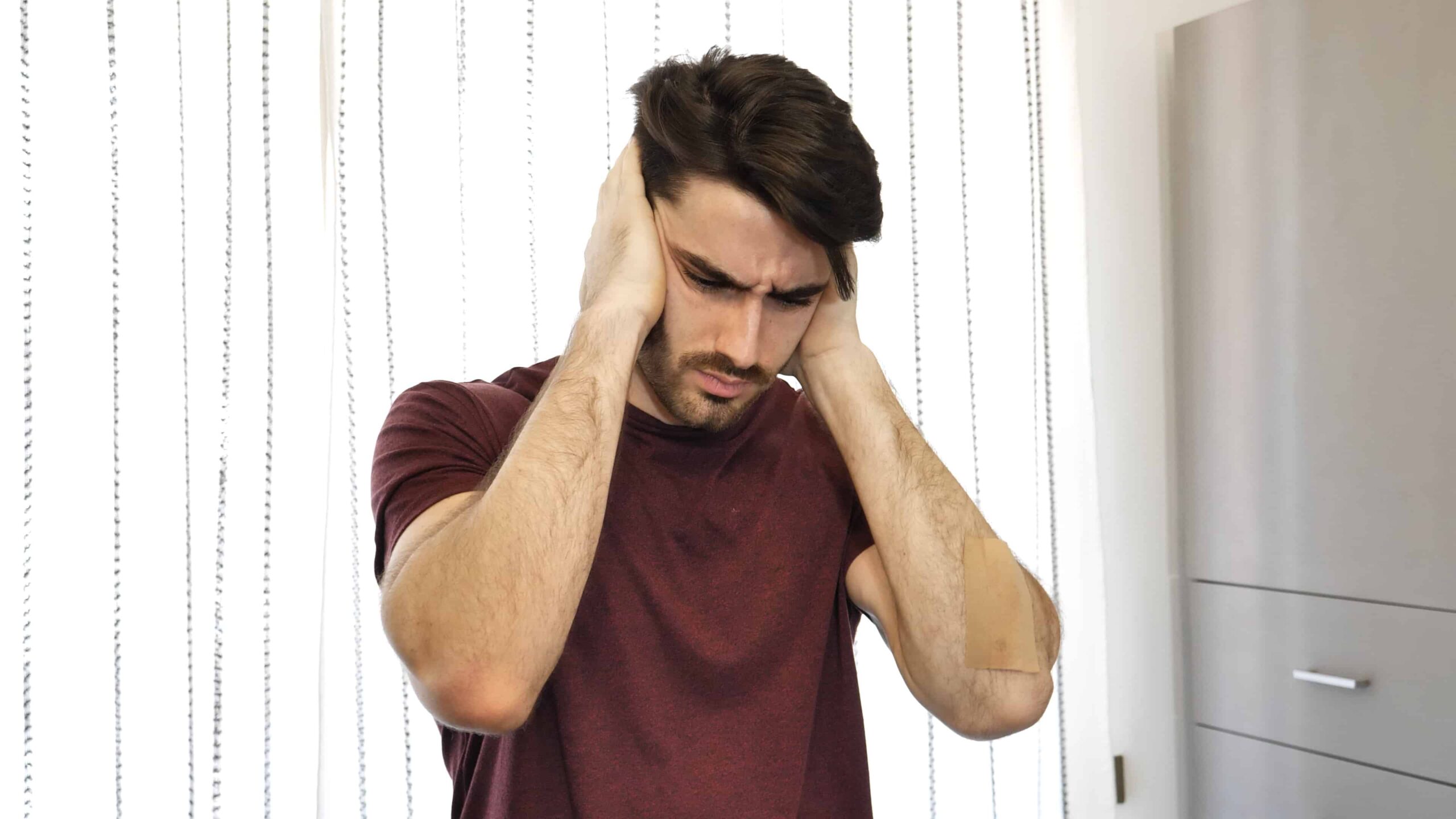 Handsome young man covering his ears, stressed or unhappy because of too much noise. Indoors shot